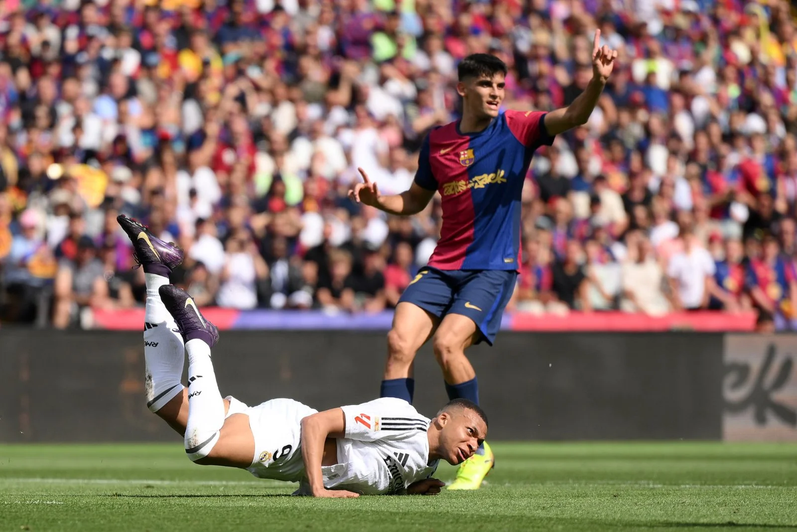 BARCELONA, SPAIN - MAY 11: Kylian Mbappe of Real Madrid falls to the floor, as Gerard Martin of FC Barcelona reacts during the LaLiga match between FC Barcelona and Real Madrid CF at Estadi Olimpic Lluis Companys on May 11, 2025 in Barcelona, Spain.